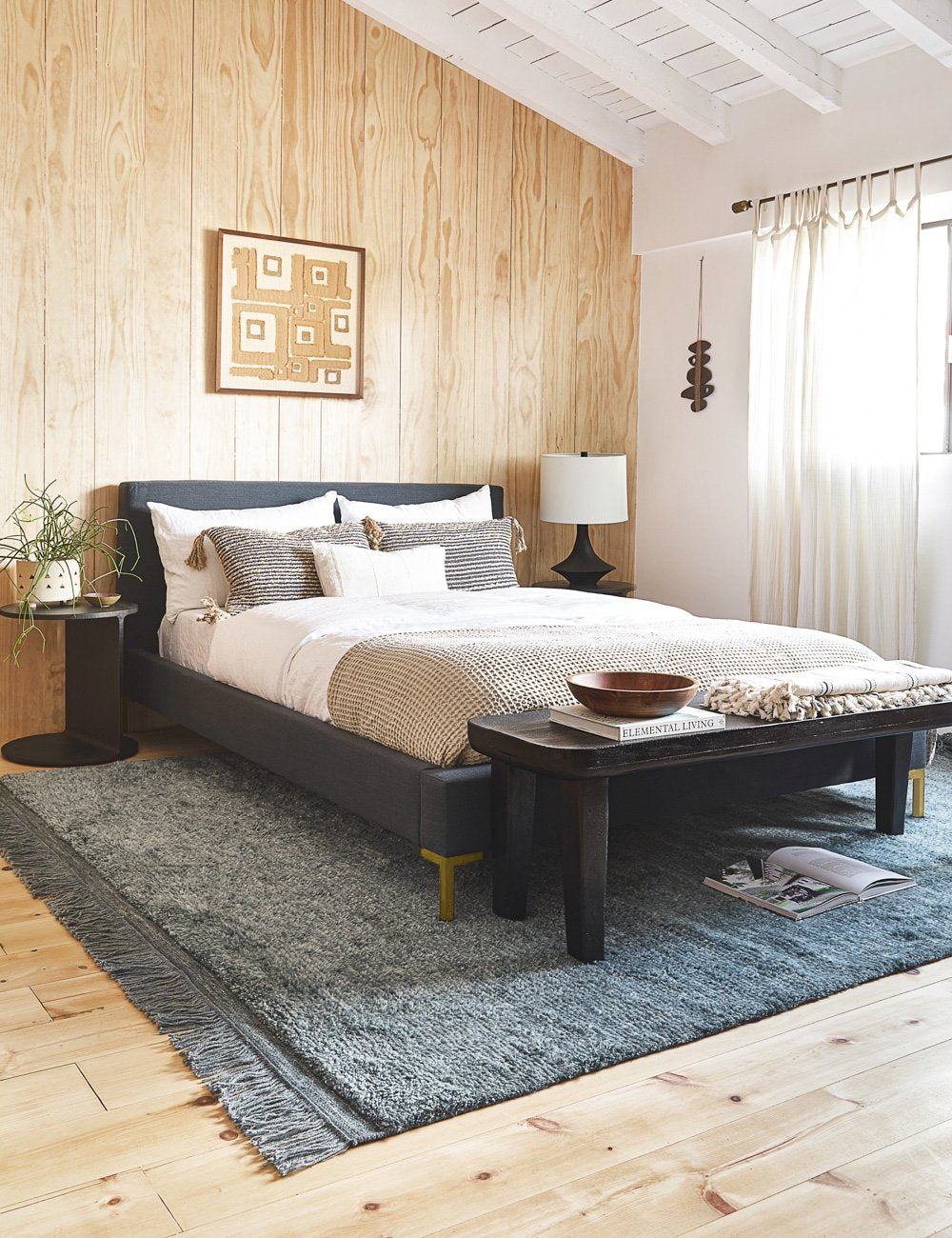 #showall::L0459268 | The Deva navy linen bed lays in a bedroom with a wooden paneled wall atop a gray fringed rug