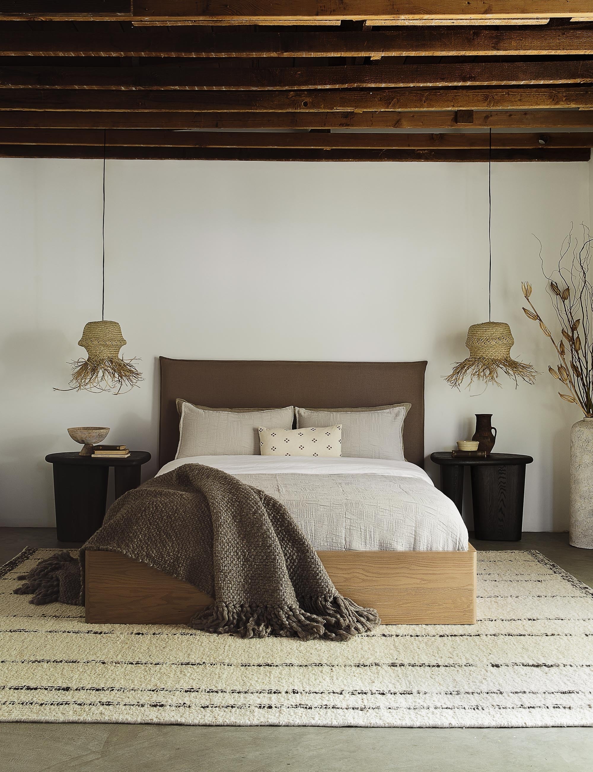 #showall::L0457336 | The Nia mushroom brown linen bed sits atop a plush rug in between two jute pendant lights under a wooden beamed ceiling