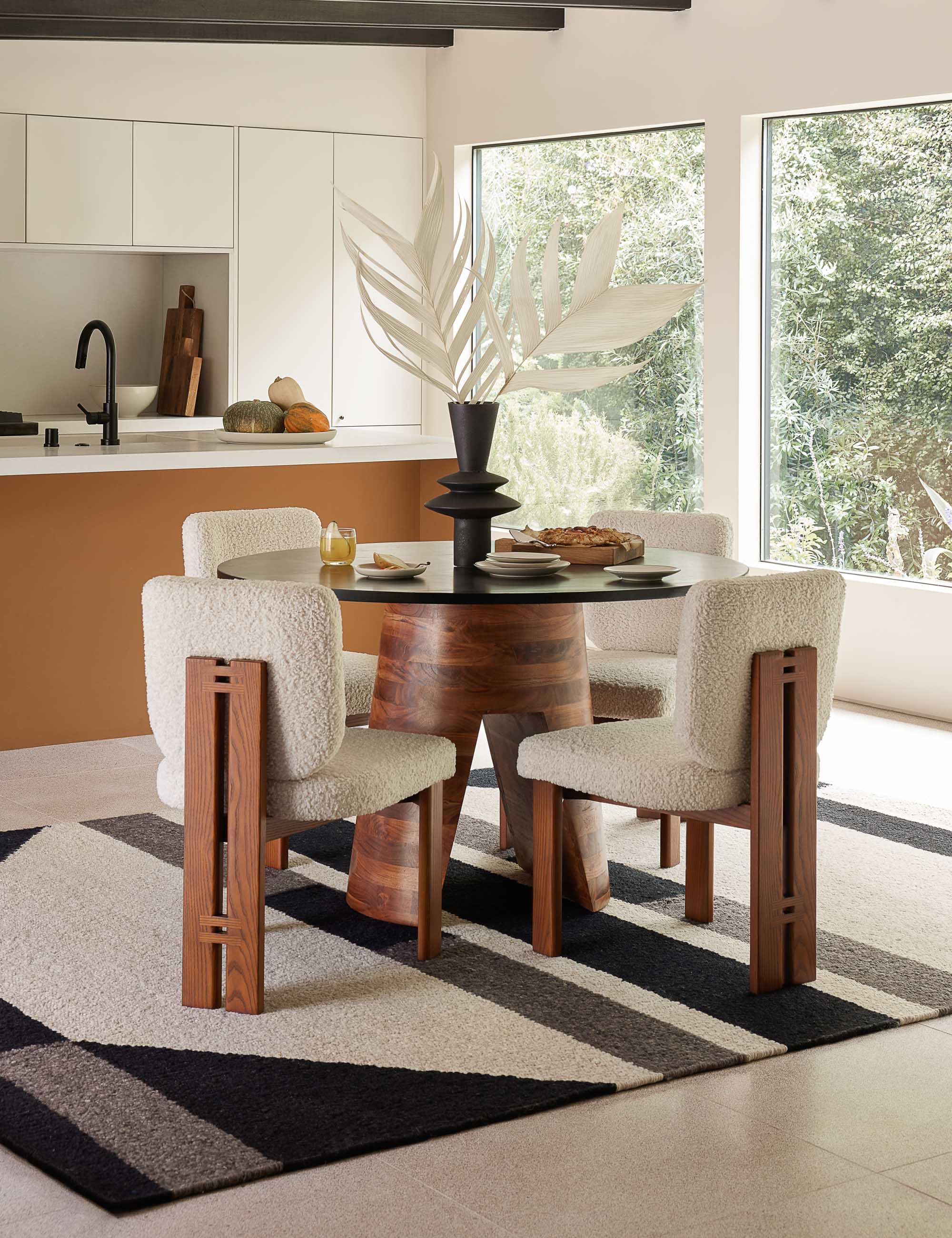#color::black-and-brown | The Adler acadia wooden round dining table sits atop a patterned carpet surrounded by four boucle dining chairs