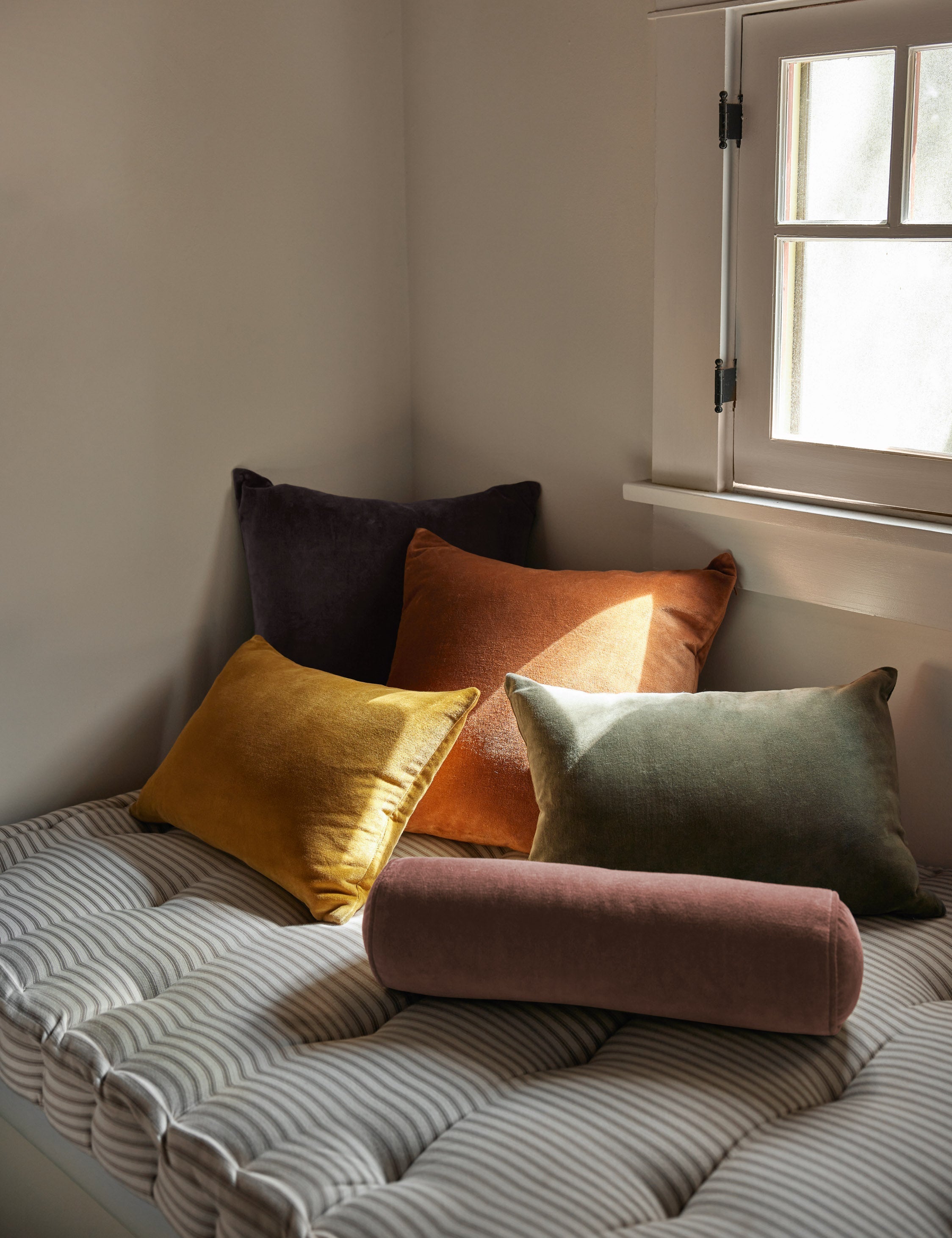 #color::moss #style::lumbar #fill type::with-feather-down-insert  #fill type::pillow-cover-only |   Charlotte velvet pillow in mustard, burnt orange, warm gray, and moss sit together on a striped cushioned bench