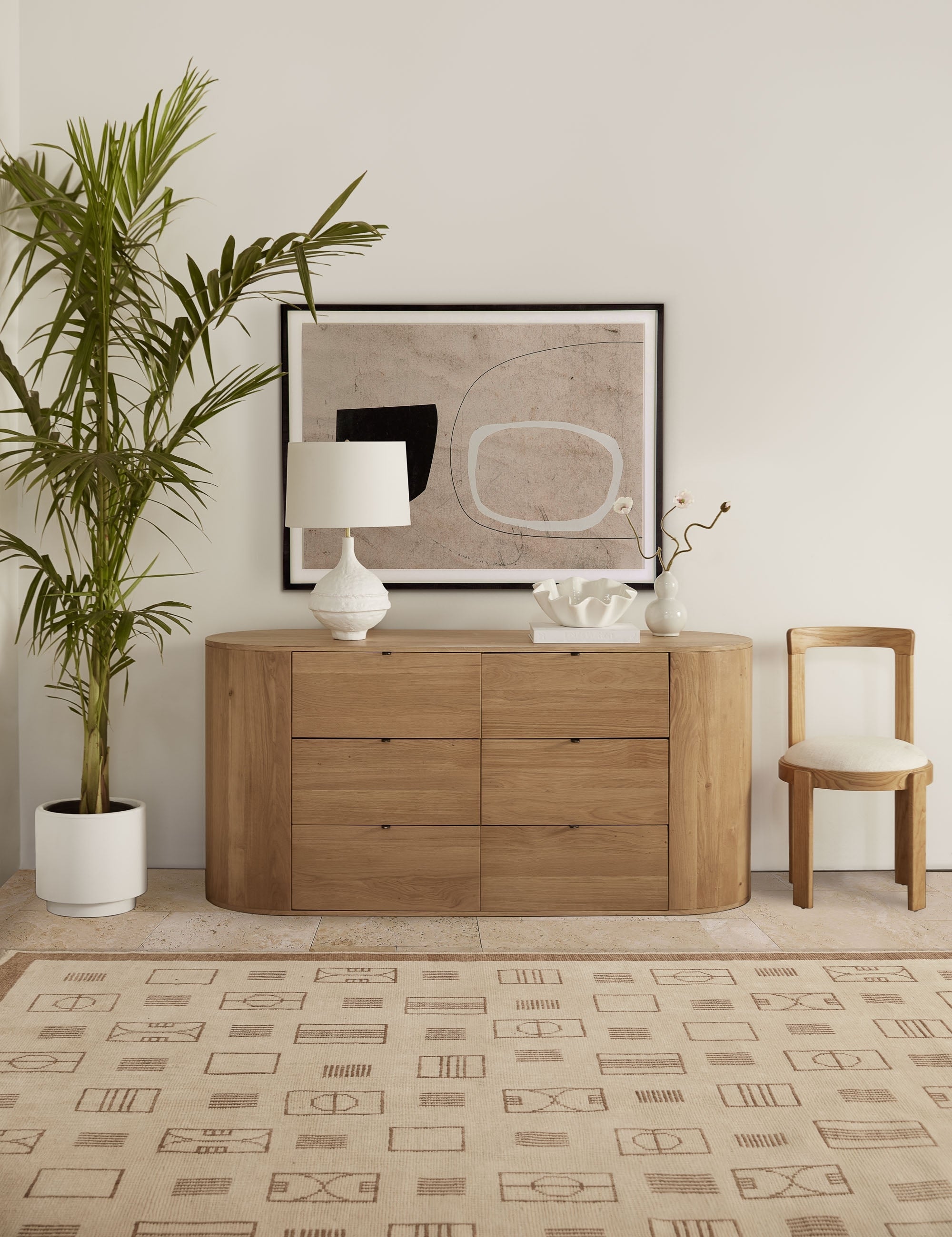 | Kono 6-drawer curved oak wide dresser styled as a sideboard decorated with a white table lamp, white ruffle bowl and modern framed artwork.